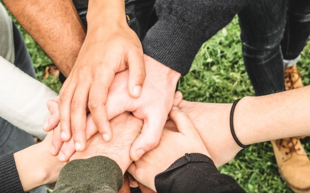 A group of diverse hands stacked together on grass.